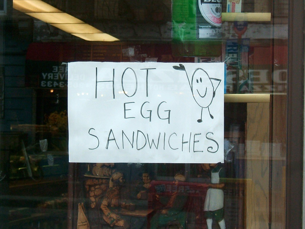 posted in a shop window, a simple sign in black sharpie on slightly rumpled white paper that says HOT EGG SANDWICHES with a cute drawing of a smiling, dancing egg

