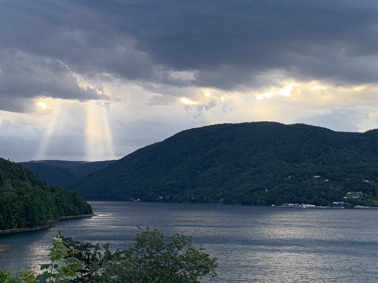 God rays beaming down through dramatic clouds, onto green mountainous terrain and a ripping lake